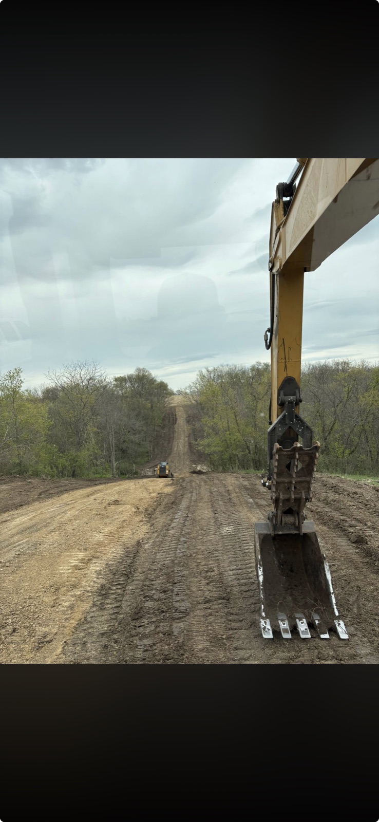 Excavator cutting and grading a new road through wooded land